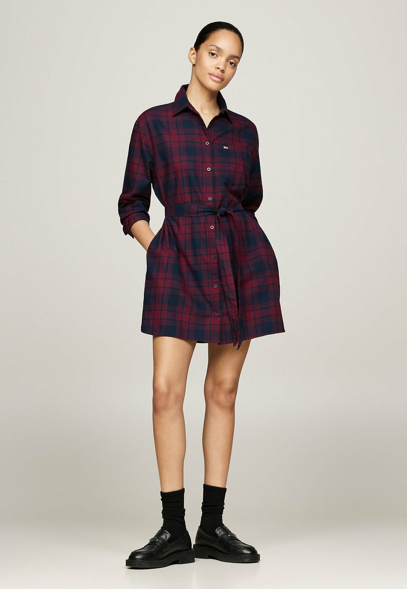 Rød og marineblå ternet skjortekjole med knaplukning, lange ærmer og bælte i taljen; har lommer og en afslappet pasform.