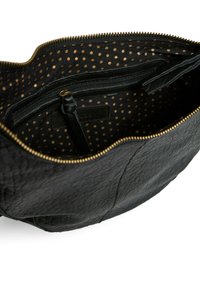Intérieur d'un sac en cuir noir avec une fermeture éclair dorée, présentant un motif à pois dorés sur un tissu noir et une petite poche zippée.