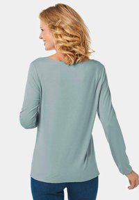 Helles blaues, langärmliges Oberteil mit weitem Ausschnitt und abgerundetem Saum. Weicher Stoff mit glatter Textur. Kombiniert mit dunkelblauen Jeans.