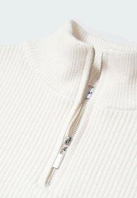 Sweter w kolorze kremowym z prążkowanym wzorem, z kołnierzem na zamek i srebrnym suwakiem. Materiał wydaje się miękki i ma teksturowane wykończenie.