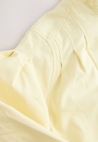 Gros plan d'un tissu jaune pâle montrant la couture d'épaule et les détails de la couture sur un vêtement doux et texturé.