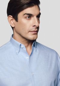 Jasnoniebieska koszula z guzikami, z wyraźnym kołnierzykiem, z delikatną fakturą i małymi guzikami. Dopasowany krój, prezentujący czysty design.