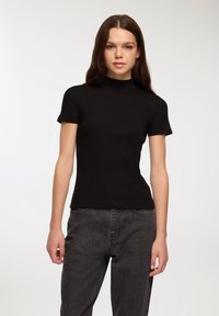 Czarny prążkowany top z krótkim rękawem i wysoką szyją, dopasowany fason, gładka tekstura, w połączeniu z ciemnoszarymi dżinsami.