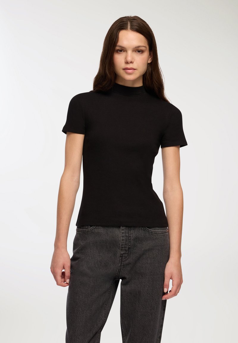 Czarny prążkowany top z krótkim rękawem i wysoką szyją, dopasowany fason, gładka tekstura, w połączeniu z ciemnoszarymi dżinsami.