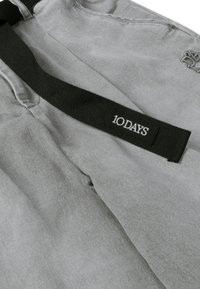 Bolsa de tela gris con textura suave, con una correa tejida negra etiquetada "10 DAYS" y detalles bordados sutiles.