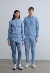 Ανοιχτό μπλε φούτερ με κουκούλα και αντίστοιχο παντελόνι φόρμας, κατασκευασμένα από μαλακό ύφασμα, με τσέπες καγκουρό και ριμπ μανσέτες. Απλός σχεδιασμός.
