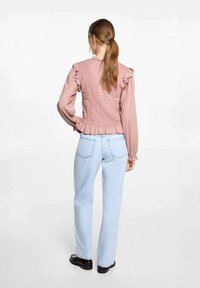 Rosa smockblus med volanger på axlarna, kombinerad med ljusblå raka jeans. Outfiten har en samlad midja och texturdetalj på ryggen.