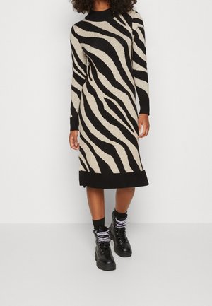 Vestido de punto con un patrón de rayas de cebra en crema y negro, con un cuello alto y puños acanalados, combinado con botas de combate negras.