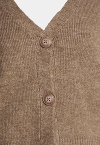 Hnědý žebrovaný svetr na zapínání s výstřihem do V a dvěma kulatými hnědými knoflíky vpředu, který se vyznačuje měkkou texturou a pleteným vzorem.