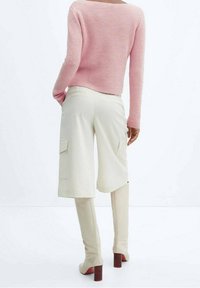 Pull en tricot rose clair avec un design cropped, associé à un short cargo crème avec deux poches latérales et des bottes beiges à hauteur de genou avec des talons carrés.