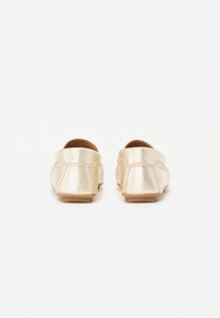 Goldene metallische Slipper mit runder Zehenpartie, flacher Sohle und glatter Lederoberfläche, die dezente Nähte und keine Hardware aufweisen.