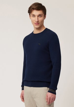 Navy blue knitted sweater with a textured pattern, round neckline, and ribbed cuffs. Small green logo on the chest.