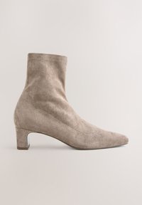 Beige suede ankle boot with a pointed toe and block heel. Features a smooth texture and minimalist design with subtle stitching details.