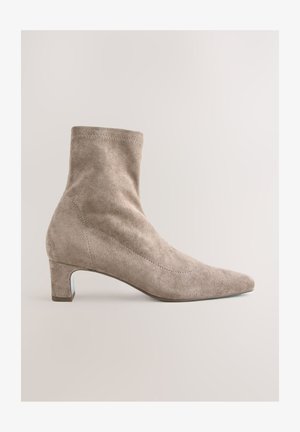 Beežist seemisnahast pahkluu saabas terava varba ja plokktallaga. Omadused on sile tekstuur ja minimalistlik disain peente õmblustega.