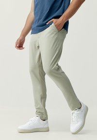 Ljusgröna slim-fit byxor med framfickor och en mjuk textur, kombinerat med vita sneakers och en blå ärmlös topp.