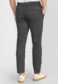 Grijze pantalon met een slim fit, elastische tailleband, twee achterzakken en subtiele textuur. Gecombineerd met witte sneakers met een tan zool.