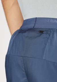 Marineblaue Sportshorts mit strukturiertem Finish, ausgestattet mit einer Reißverschlusstasche und Netzpartien am Bund für Atmungsaktivität.