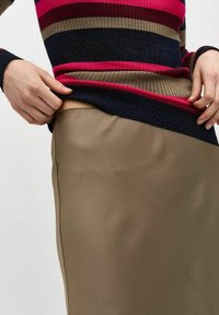 Maglione a righe e costine rosso, blu navy e khaki, abbinato a una goniella liscia color marrone chiaro. Cuciture evidenti sul lato della goniella.