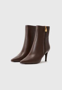Bottines en cuir marron avec des bouts pointus, des talons fins et une fermeture éclair sur le côté avec un accent doré. Texture lisse et design élégant.