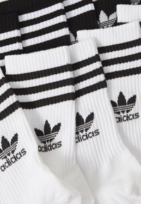 Chaussettes rayées noir et blanc en tissu côtelé, arborant le logo Adidas et trois rayures horizontales en haut.