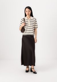Randig krämfärgad polo-shirt med krage och knappar, i kombination med en lång svart satinkjol. Bärs med svarta sandaler med remmar och en liten brun väska.