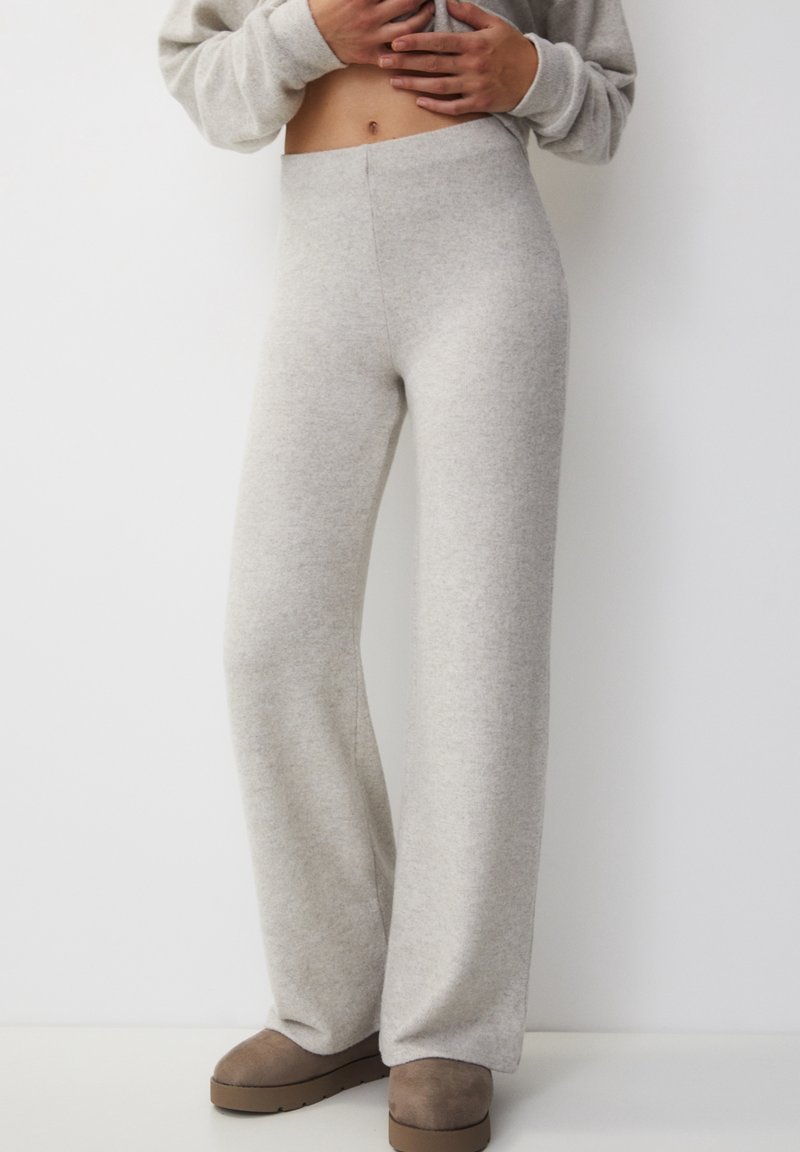 Pantalones de pierna ancha de color gris claro, fabricados en una tela suave con cintura elástica. Presentan una textura lisa y un diseño minimalista.