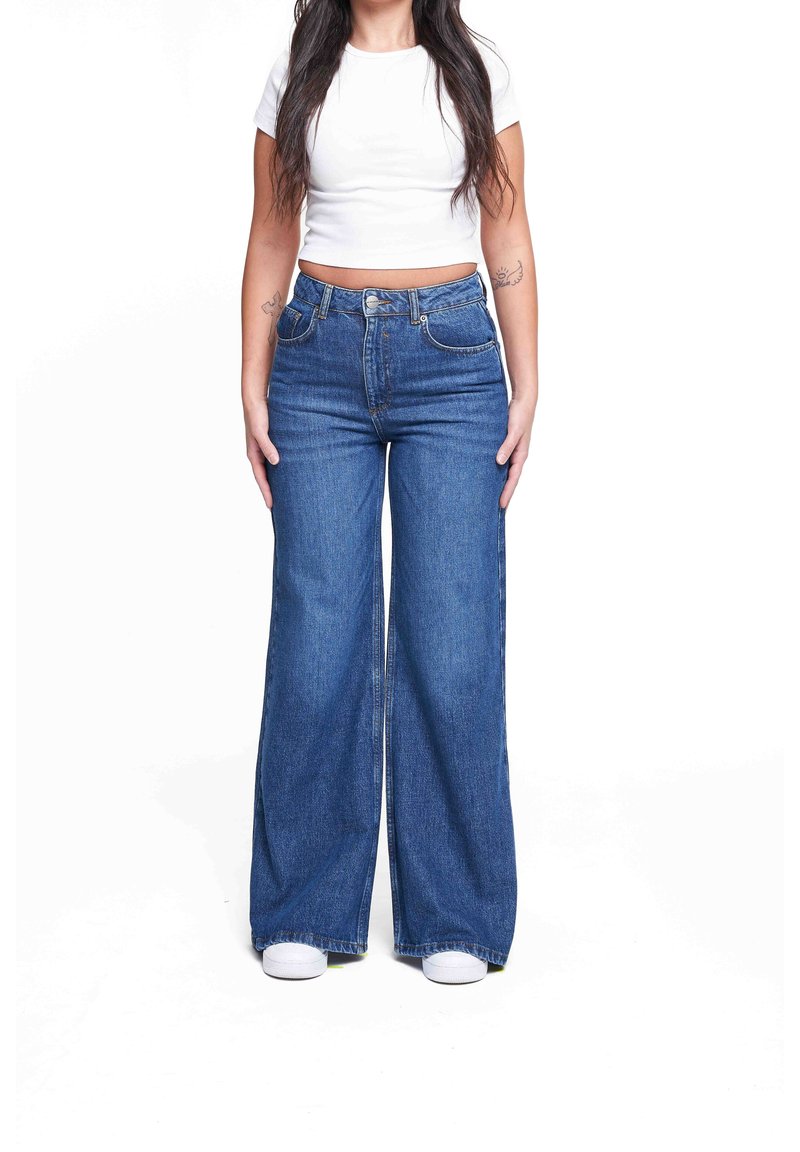 Jeans de mezclilla de tiro alto y pierna ancha, en color azul, con bolsillos delanteros y cierre de botón, con una textura suave y un acabado limpio.