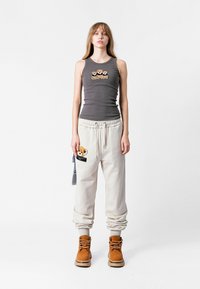 Camiseta sin mangas gris con un parche decorativo de oso, combinada con joggers crema que tienen un aplique de oso, y botas de cordones en color marrón anaranjado.