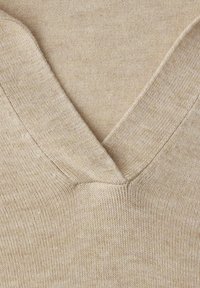 Gros plan sur un tissu tricoté beige avec un col en V et une texture côtelée détaillée.