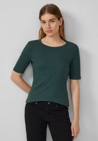 Donkergroen geribbelde t-shirt met een ronde hals en korte mouwen, gecombineerd met zwarte jeans. Heeft een getailleerd ontwerp en een gladde textuur.