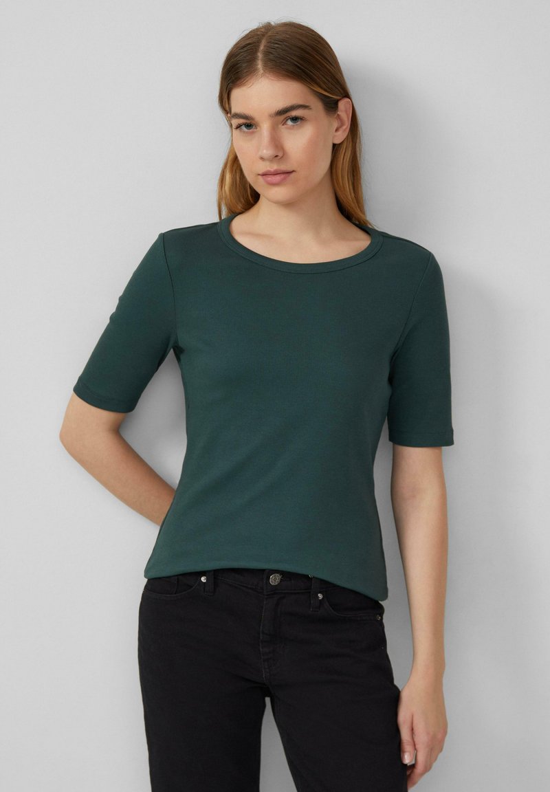 Donkergroen geribbelde t-shirt met een ronde hals en korte mouwen, gecombineerd met zwarte jeans. Heeft een getailleerd ontwerp en een gladde textuur.