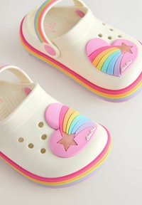 Valged klotsid, millel ees on roosa süda ja vikerkaare kujundus, ääristatud värviliste triipudega ümber tallapea. Varustatud sobiva tagarihmaga.