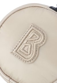 Borsa rotonda beige con un prominente logo "B" ricamato in un design testurizzato. Tessuto liscio con dettagli cuciti attorno al logo.