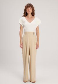 Witte v-hals top met textuur en pofmouwen, gecombineerd met hooggetailleerde, lichtbeige wijde broek en nude hakken.