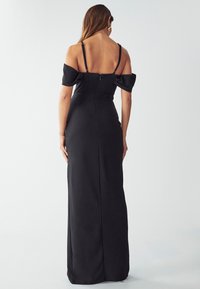 Abito da sera nero off-shoulder con silhouette aderente, chiusura a zip sul retro e tessuto fluido. Lunghezza lunga con texture morbida.