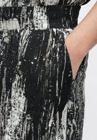 Schwarz-weißes Stoffmaterial mit abstraktem, streifigem Muster; verfügt über einen elastischen Bund und eine Seitentasche für ein funktionales Design.