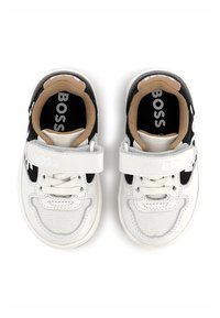 Sneaker bianche e nere con una chiusura in velcro, caratterizzate da una finitura testurizzata e un interno color testa di moro a contrasto, etichettate "BOSS" all'interno.
