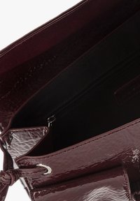 Burgundzka torebka na patentowanej skórze o gładkiej fakturze, z zamykanym na zamek przedziałem i metalowymi akcentami. Wnętrze jest widoczne.