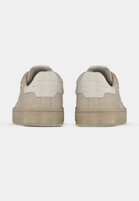 Beige Wildledersneaker mit strukturiertem Design, hellfarbiger glatter Ferse, flacher Sohle und Zuglasche hinten.