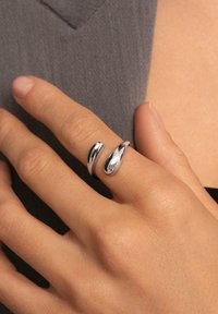 Anillo doble de plata en una mano, con curvas elegantes y suaves y un acabado pulido. El diseño tiene una forma contemporánea y minimalista.