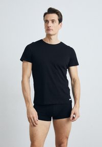 T-shirt noir ajusté en coton avec des manches courtes, col rond et une petite étiquette logo sur le bas de l'ourlet, associé à un boxer noir.