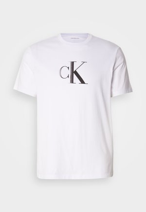 Valkoinen puuvillapaidassa on näyttävä musta 'cK'-logo rohkealla fontilla etuosassa. Lyhyt hihainen malli klassisella pyöreällä pääntiellä.