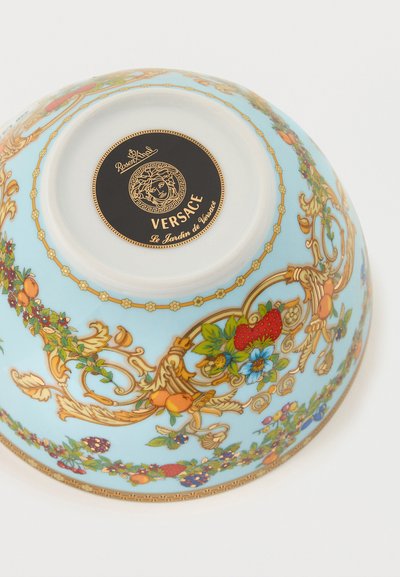 Ανάποδο παστέλ γαλάζιο μπολ με περίτεχνα χρυσά, φρουτώδη και λουλουδάτα μοτίβα και μαύρη ετικέτα Versace στο κάτω μέρος.