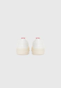 Hvide lædersneakers med en tykkere cremefarvet sål, der har røde detaljer ved hælen. Glat tekstur og afrundet design.