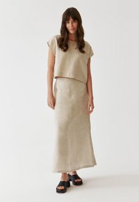 Linen two-piece outfit in light beige with a cropped top and long skirt. Model wears chunky black sandals with open toes. Simple, relaxed fit.