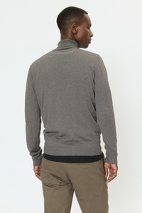 Pilkas megztinis iš mezgimo su aukštu kaklu, prigludusiomis rankogaliais ir raštuotu juosmeniu. Audinys atrodo minkštas ir lygus.