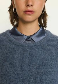 Tumesinine kootud sviiter tekstuuriga viimistlusega, millele on lisatud tumedast sinisest siidist särgikaelus, millel on nööpide kinnitamine.