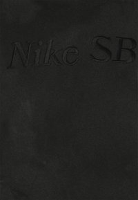 Tissu noir avec une broderie discrète et en relief du texte "Nike SB" en fil noir assorti.
