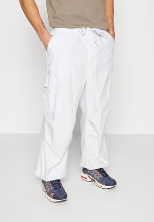Pantaloni cargo bianchi con vita regolabile, gamba larga e tasche laterali, abbinati a sneakers navy con dettagli rosa e grigio.