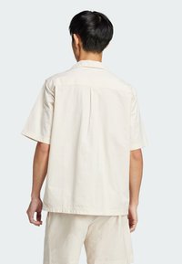 Short-sleeve, light cream shirt, textured fabric, relaxed fit, buttoned back yoke, simple collar, pairs with matching shorts.
